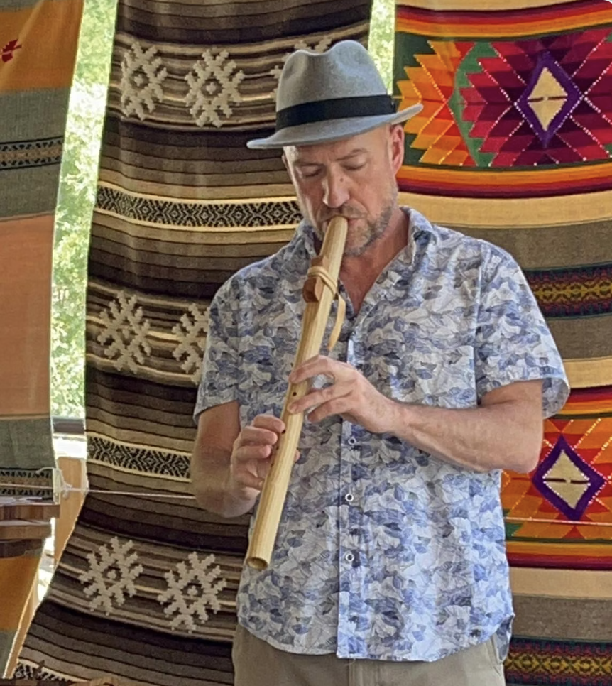 Robert playing a finished cedar flute, eyes closed, framed by traditional woven blankets