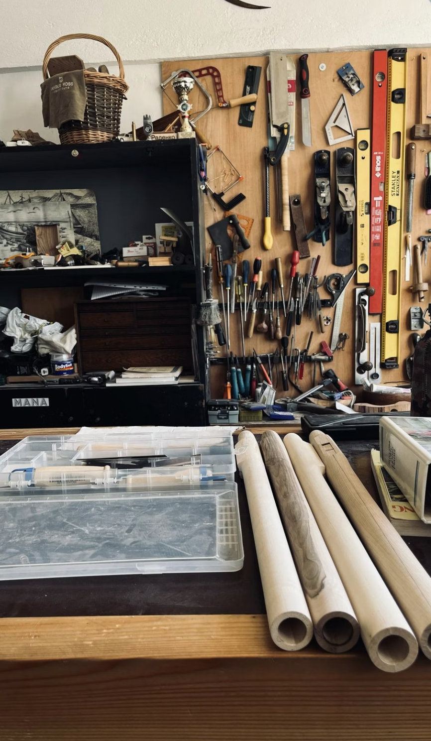 Inside Radenko's Rhodope workshop — a wooden bench with four hand-bored flute blanks beside a wall of carving tools